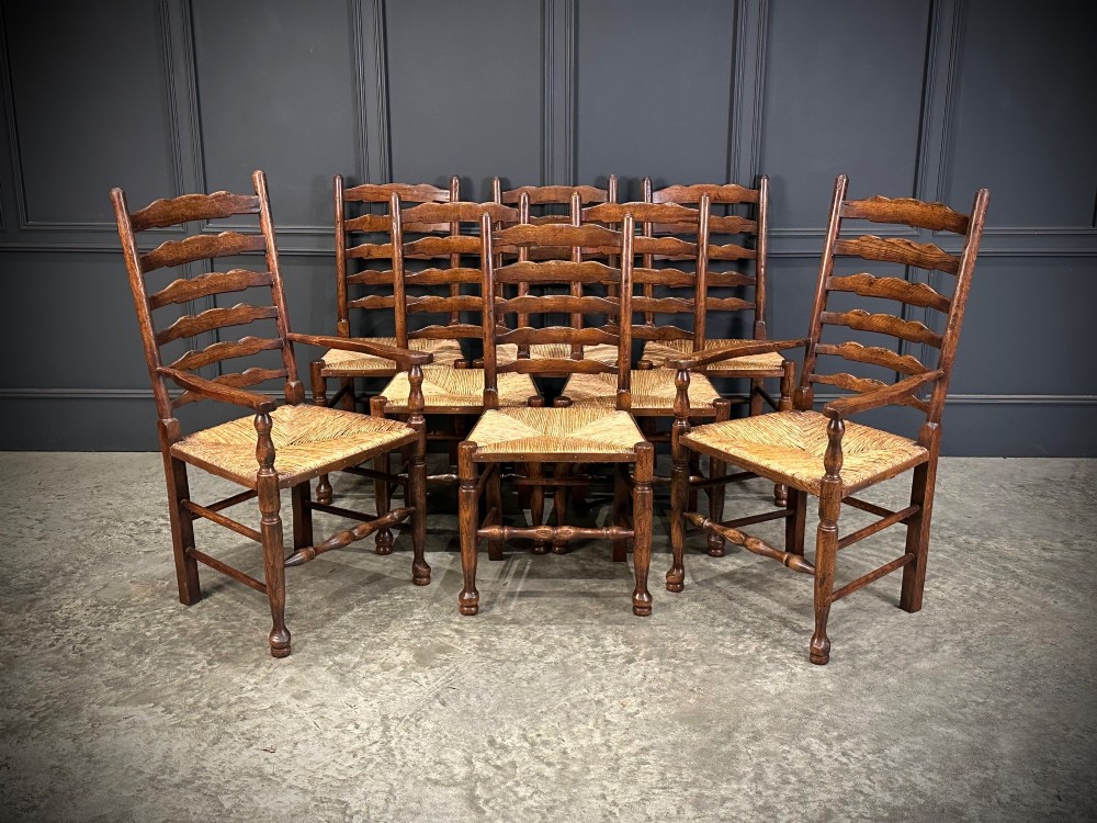 A set of eight dark oak ladder back dining chairs featuring woven rush seats, shaped back slats, and turned front legs.