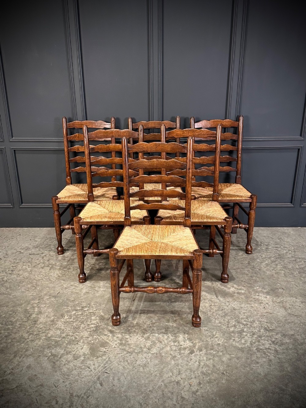 A set of eight dark oak ladder back dining chairs featuring woven rush seats, shaped back slats, and turned front legs. View II