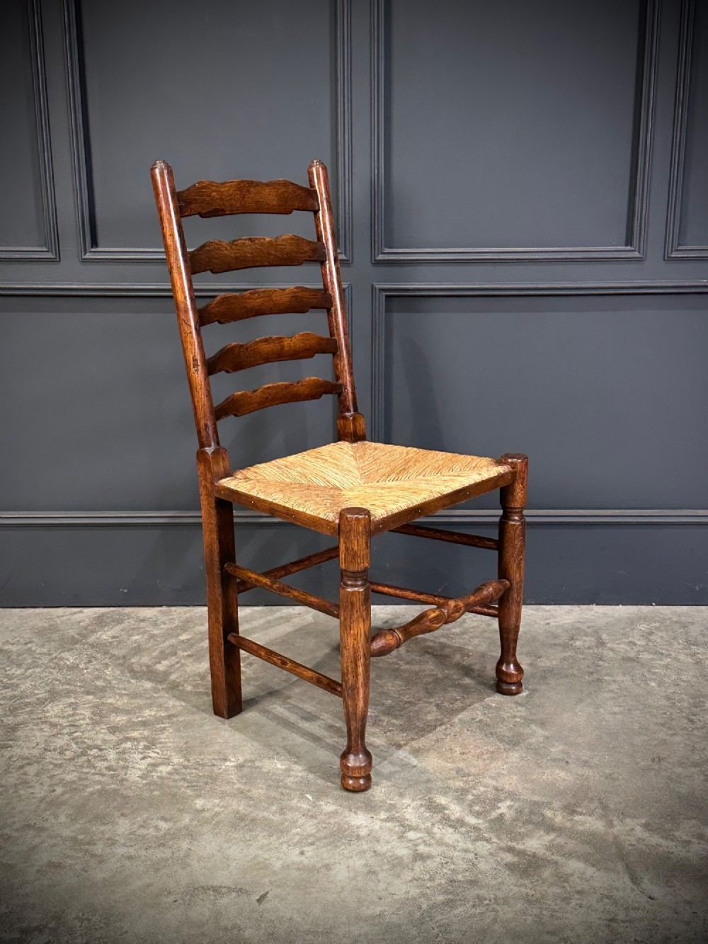 A set of eight dark oak ladder back dining chairs featuring woven rush seats, shaped back slats, and turned front legs. View III