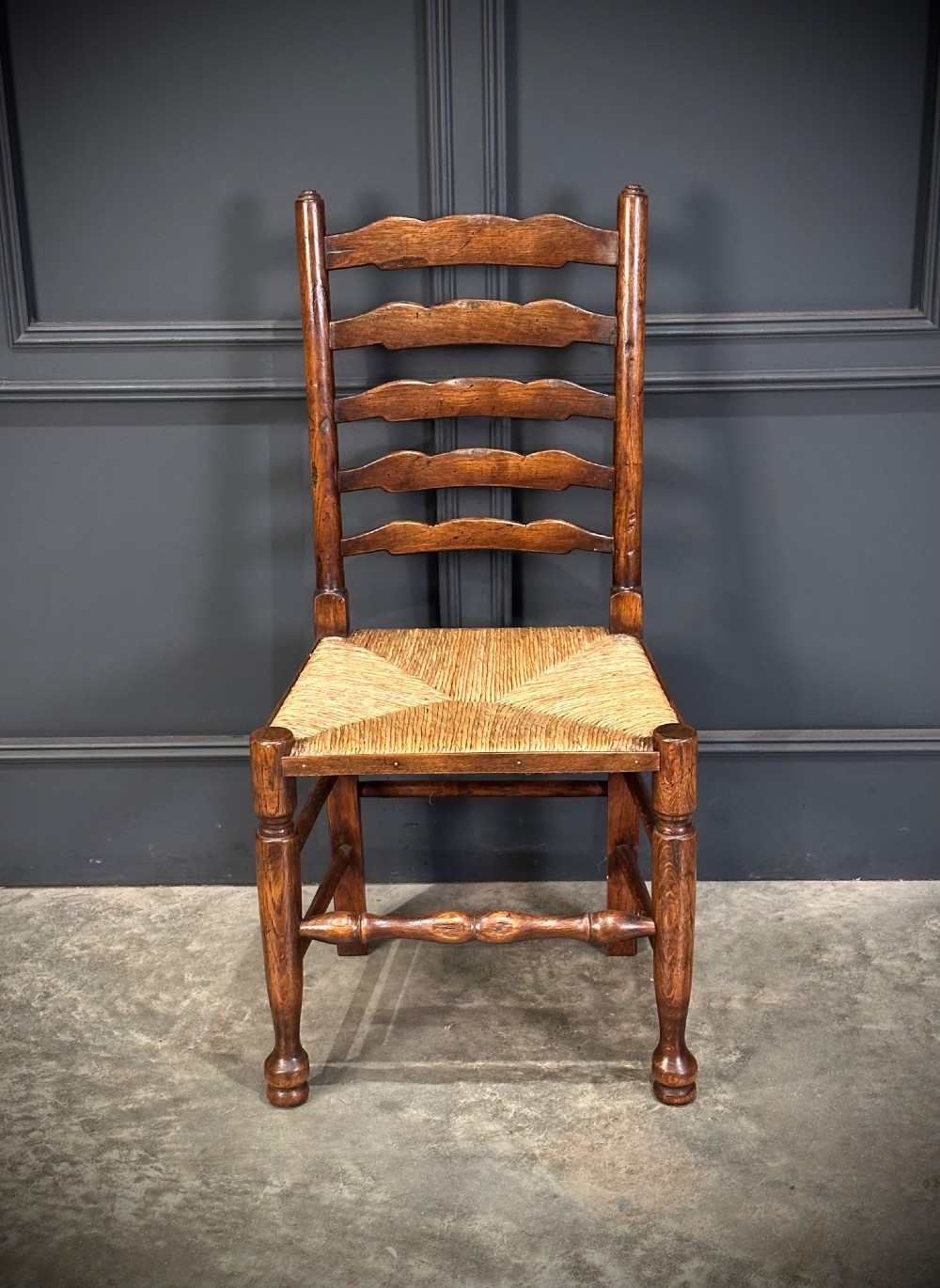 A set of eight dark oak ladder back dining chairs featuring woven rush seats, shaped back slats, and turned front legs. View IV