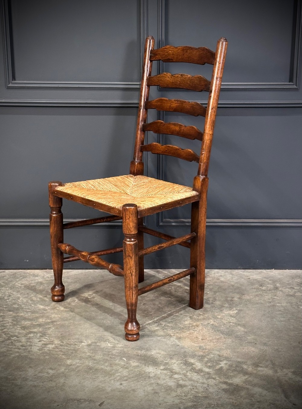 A set of eight dark oak ladder back dining chairs featuring woven rush seats, shaped back slats, and turned front legs. View V