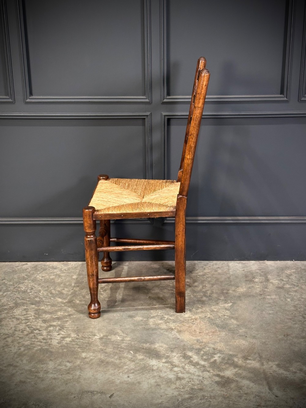 A set of eight dark oak ladder back dining chairs featuring woven rush seats, shaped back slats, and turned front legs. View VI