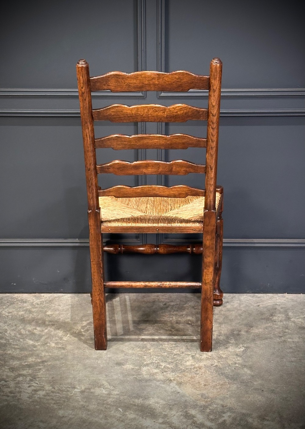 A set of eight dark oak ladder back dining chairs featuring woven rush seats, shaped back slats, and turned front legs. View VII