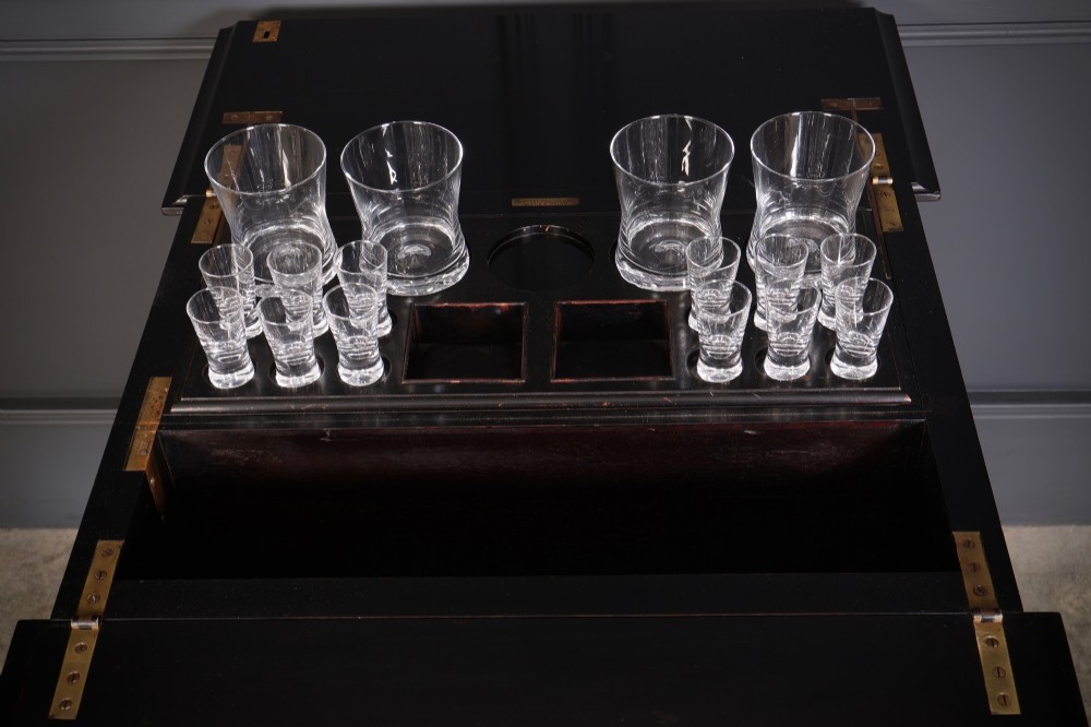 An ebonised wooden mechanical drinks table featuring opening top leaves that elevate a tray set with clear glassware, resting on tapered legs with brass castors. View IV