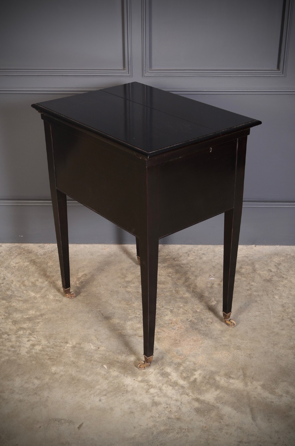 An ebonised wooden mechanical drinks table featuring opening top leaves that elevate a tray set with clear glassware, resting on tapered legs with brass castors. View IX