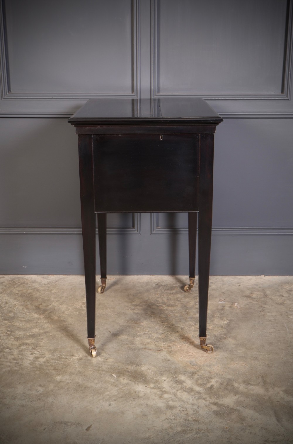 An ebonised wooden mechanical drinks table featuring opening top leaves that elevate a tray set with clear glassware, resting on tapered legs with brass castors. View X