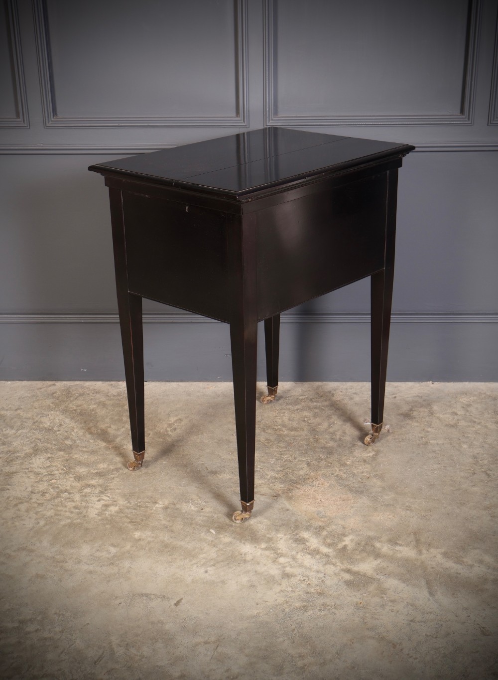 An ebonised wooden mechanical drinks table featuring opening top leaves that elevate a tray set with clear glassware, resting on tapered legs with brass castors. View XI