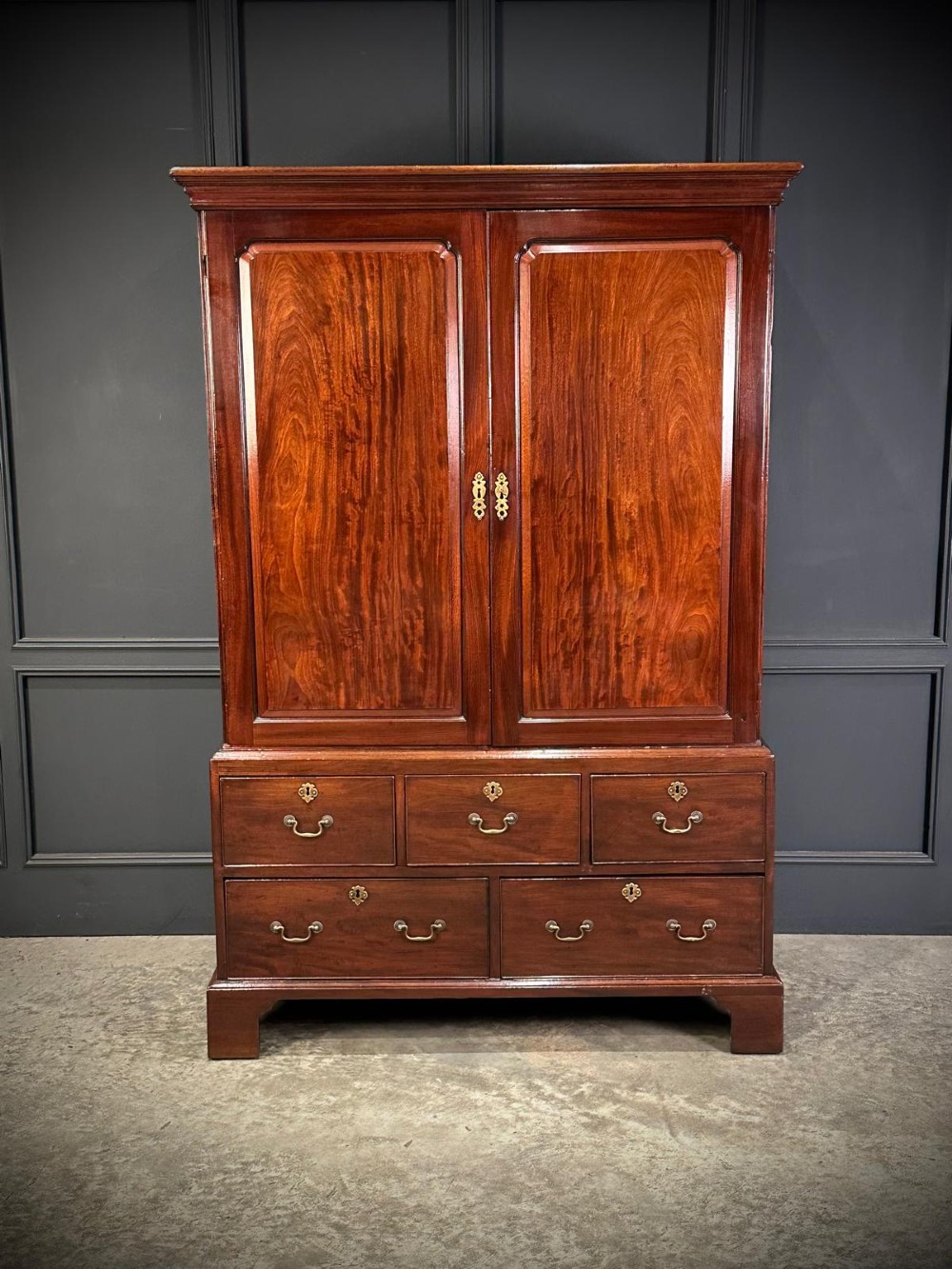 An antique Georgian mahogany gentlemans wardrobe featuring panelled upper cupboard doors above five lower drawers with brass swan-neck handles, resting on bracket feet. View III