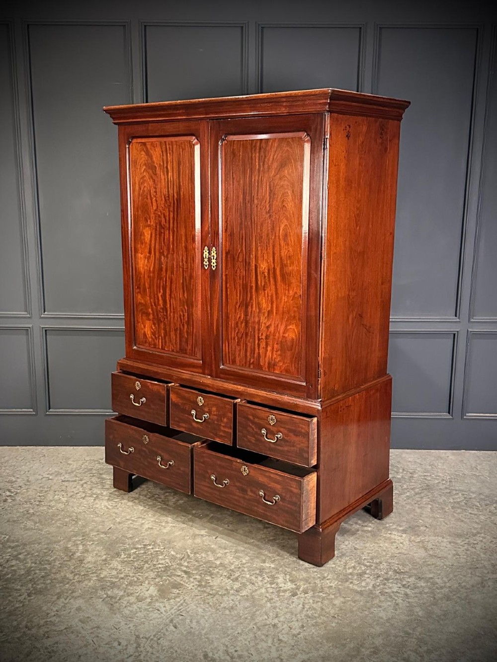 An antique Georgian mahogany gentlemans wardrobe featuring panelled upper cupboard doors above five lower drawers with brass swan-neck handles, resting on bracket feet. View IV
