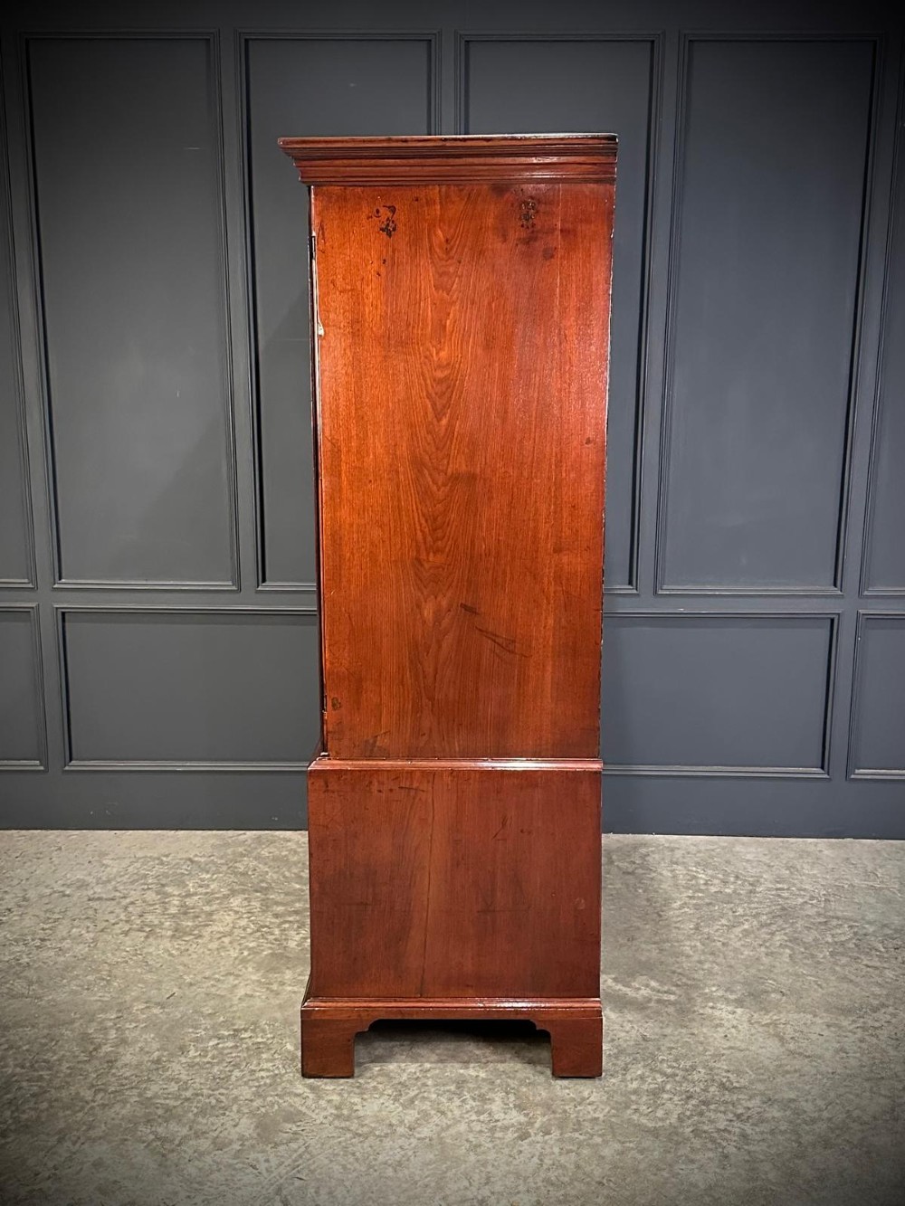 An antique Georgian mahogany gentlemans wardrobe featuring panelled upper cupboard doors above five lower drawers with brass swan-neck handles, resting on bracket feet. View V