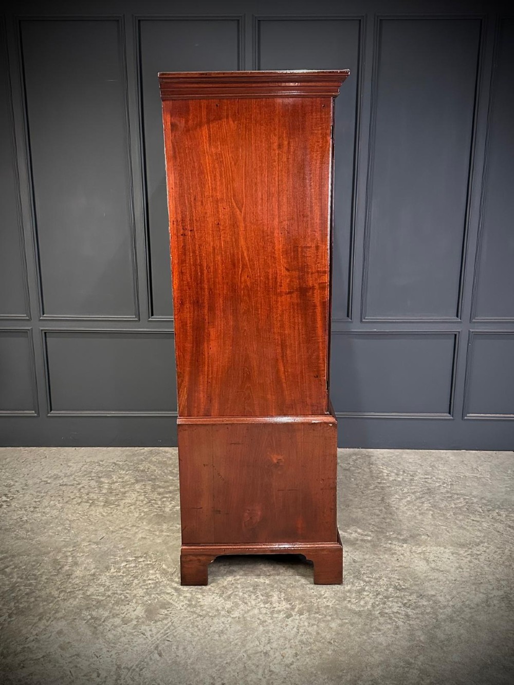 An antique Georgian mahogany gentlemans wardrobe featuring panelled upper cupboard doors above five lower drawers with brass swan-neck handles, resting on bracket feet. View VII