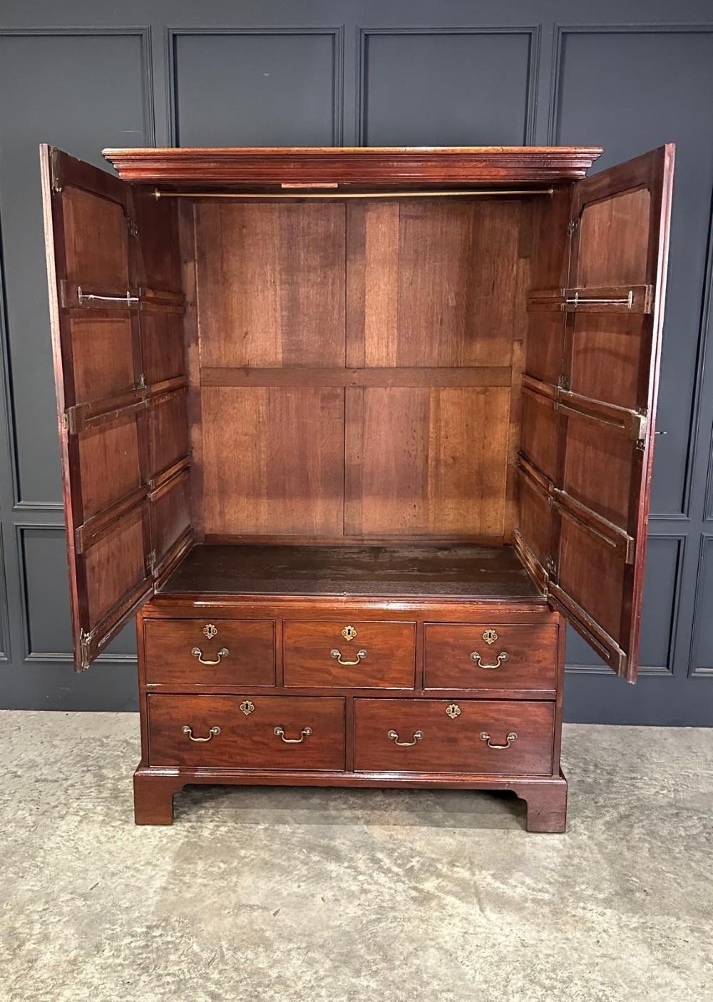 An antique Georgian mahogany gentlemans wardrobe featuring panelled upper cupboard doors above five lower drawers with brass swan-neck handles, resting on bracket feet. View VIII