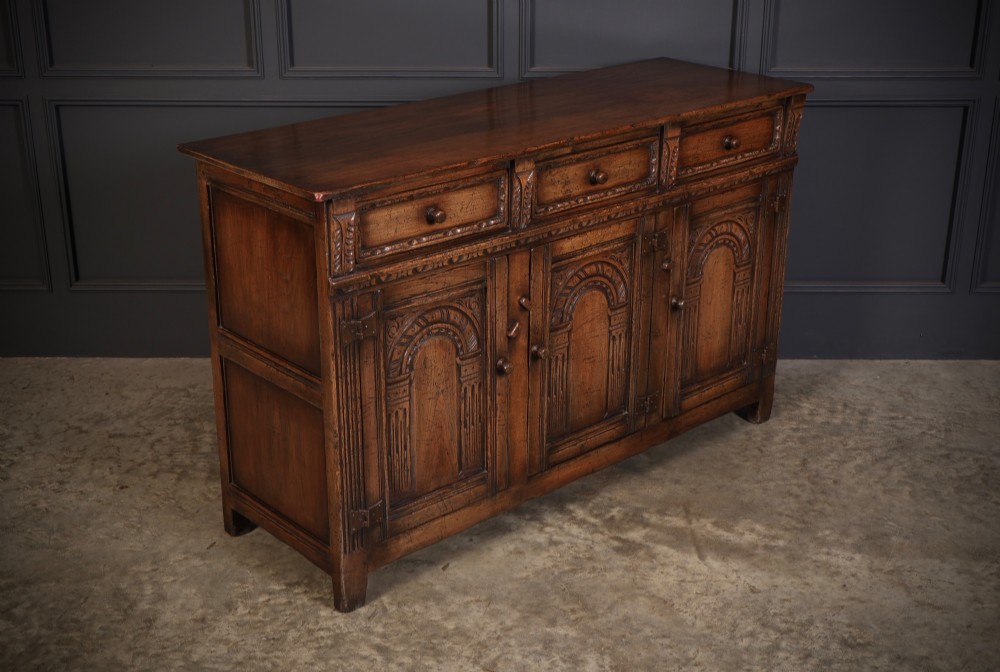 A solid oak sideboard featuring three upper drawers over four cupboard doors with carved roundhead arches and turned wooden handles. View II