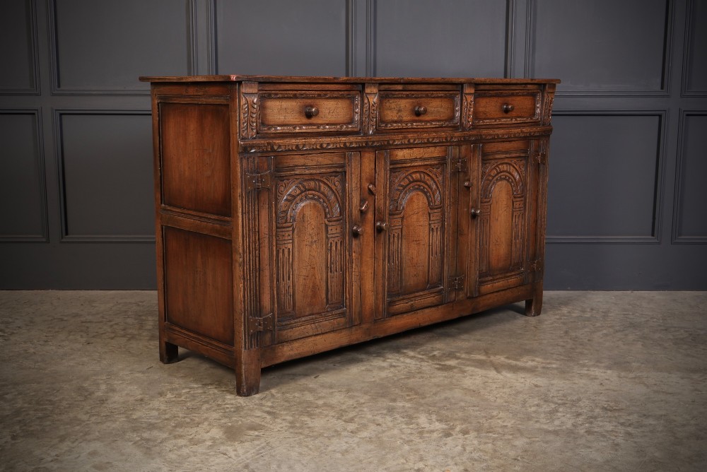 A solid oak sideboard featuring three upper drawers over four cupboard doors with carved roundhead arches and turned wooden handles.