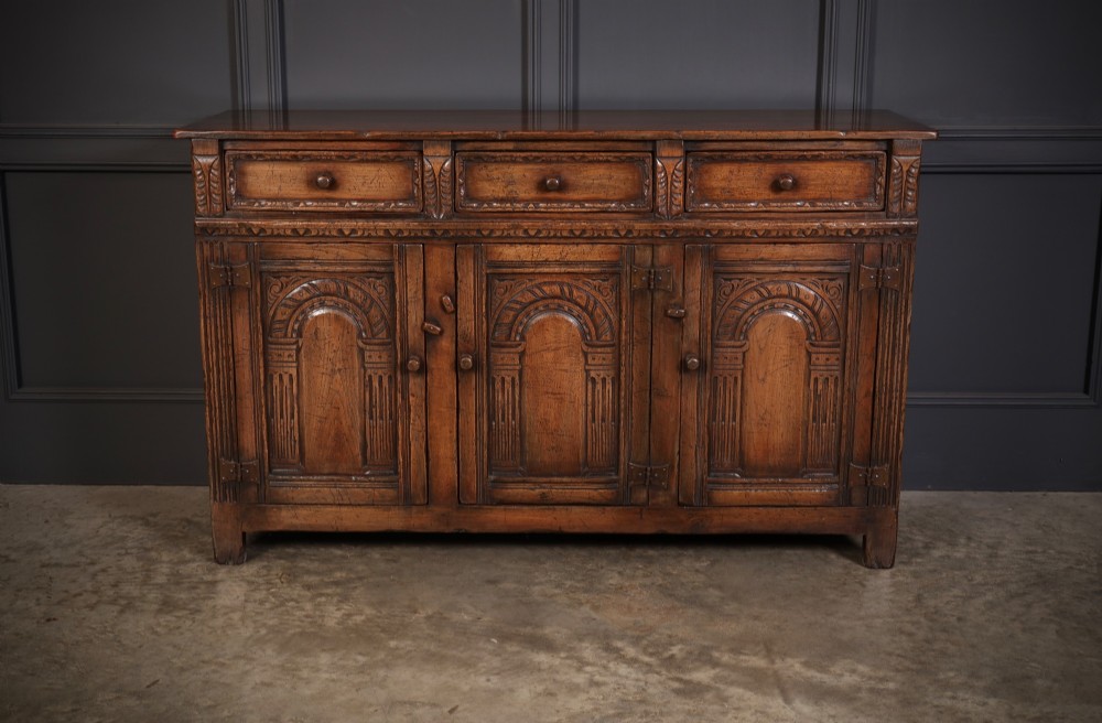 A solid oak sideboard featuring three upper drawers over four cupboard doors with carved roundhead arches and turned wooden handles. View III