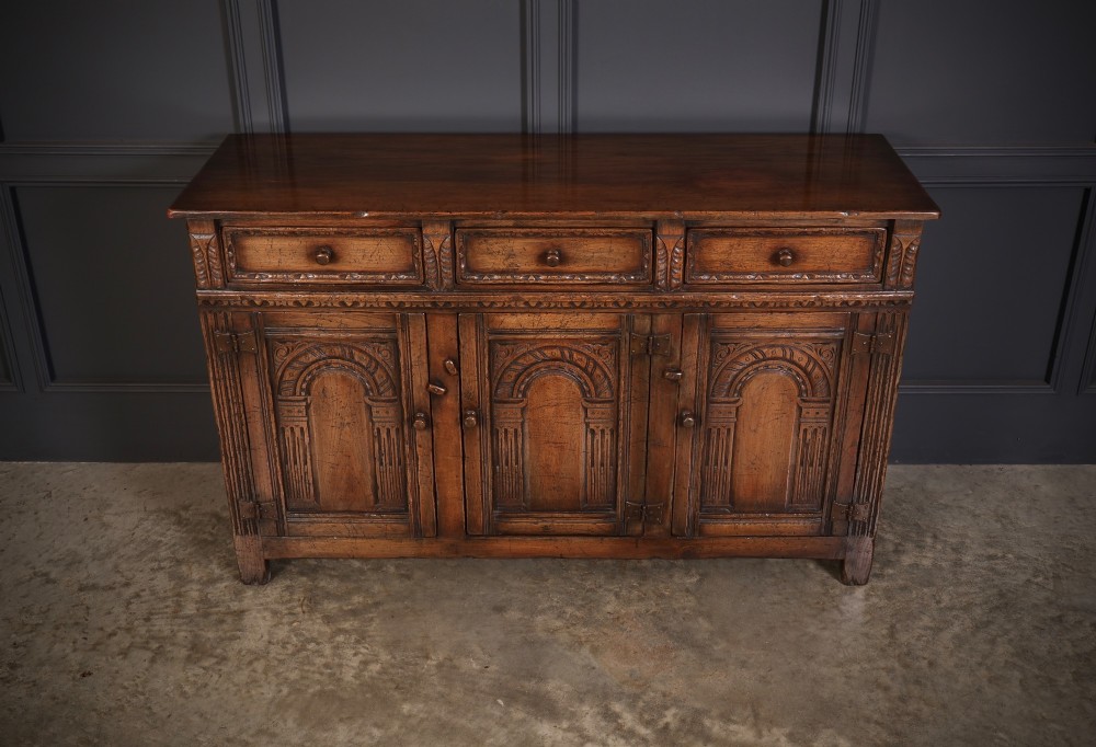 A solid oak sideboard featuring three upper drawers over four cupboard doors with carved roundhead arches and turned wooden handles. View IV