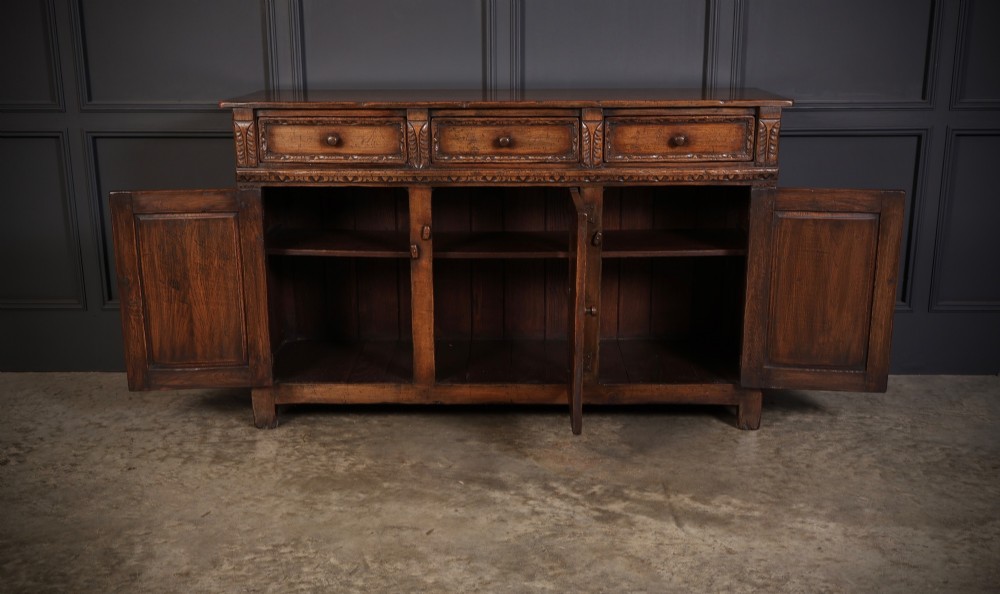 A solid oak sideboard featuring three upper drawers over four cupboard doors with carved roundhead arches and turned wooden handles. View V
