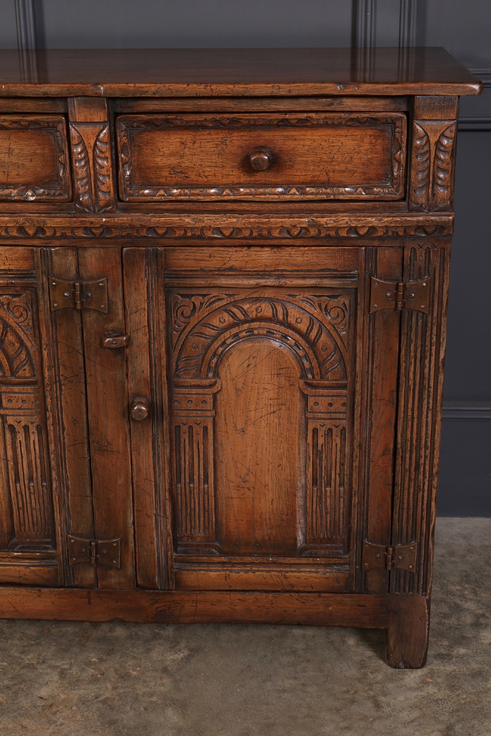 A solid oak sideboard featuring three upper drawers over four cupboard doors with carved roundhead arches and turned wooden handles. View VI