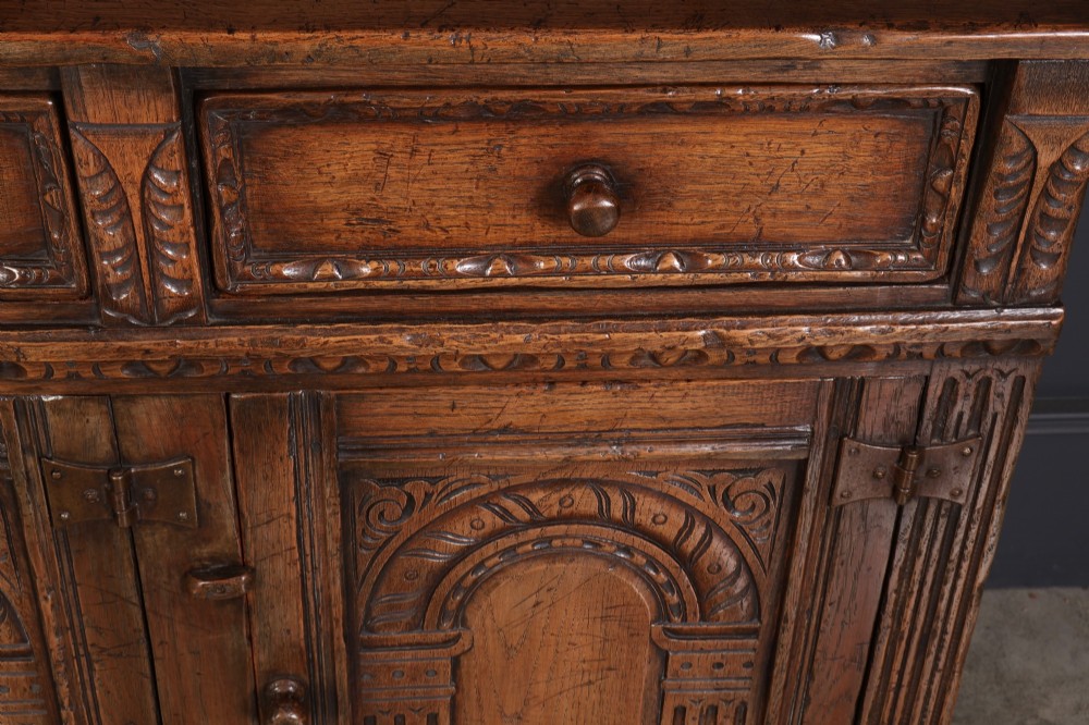 A solid oak sideboard featuring three upper drawers over four cupboard doors with carved roundhead arches and turned wooden handles. View VII
