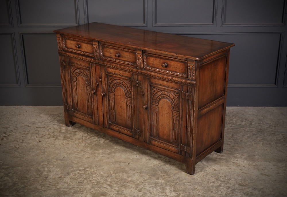 A solid oak sideboard featuring three upper drawers over four cupboard doors with carved roundhead arches and turned wooden handles. View VIII