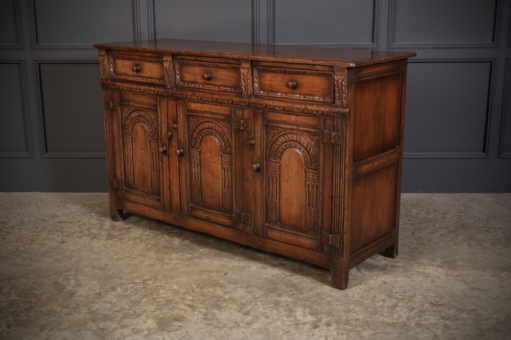 A solid oak sideboard featuring three upper drawers over four cupboard doors with carved roundhead arches and turned wooden handles. View IX