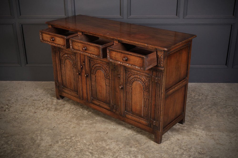 A solid oak sideboard featuring three upper drawers over four cupboard doors with carved roundhead arches and turned wooden handles. View X