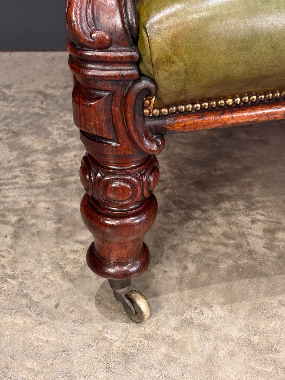 A Victorian double spoon-back settee upholstered in deep buttoned green leather with a carved mahogany frame set on brass castors. View V