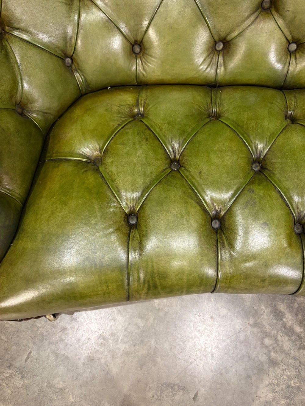 A Victorian double spoon-back settee upholstered in deep buttoned green leather with a carved mahogany frame set on brass castors. View VII
