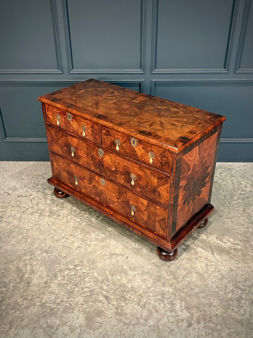 A seventeenth-century kingwood chest of drawers featuring geometric oyster veneering, brass teardrop handles, and turned bun feet. View V