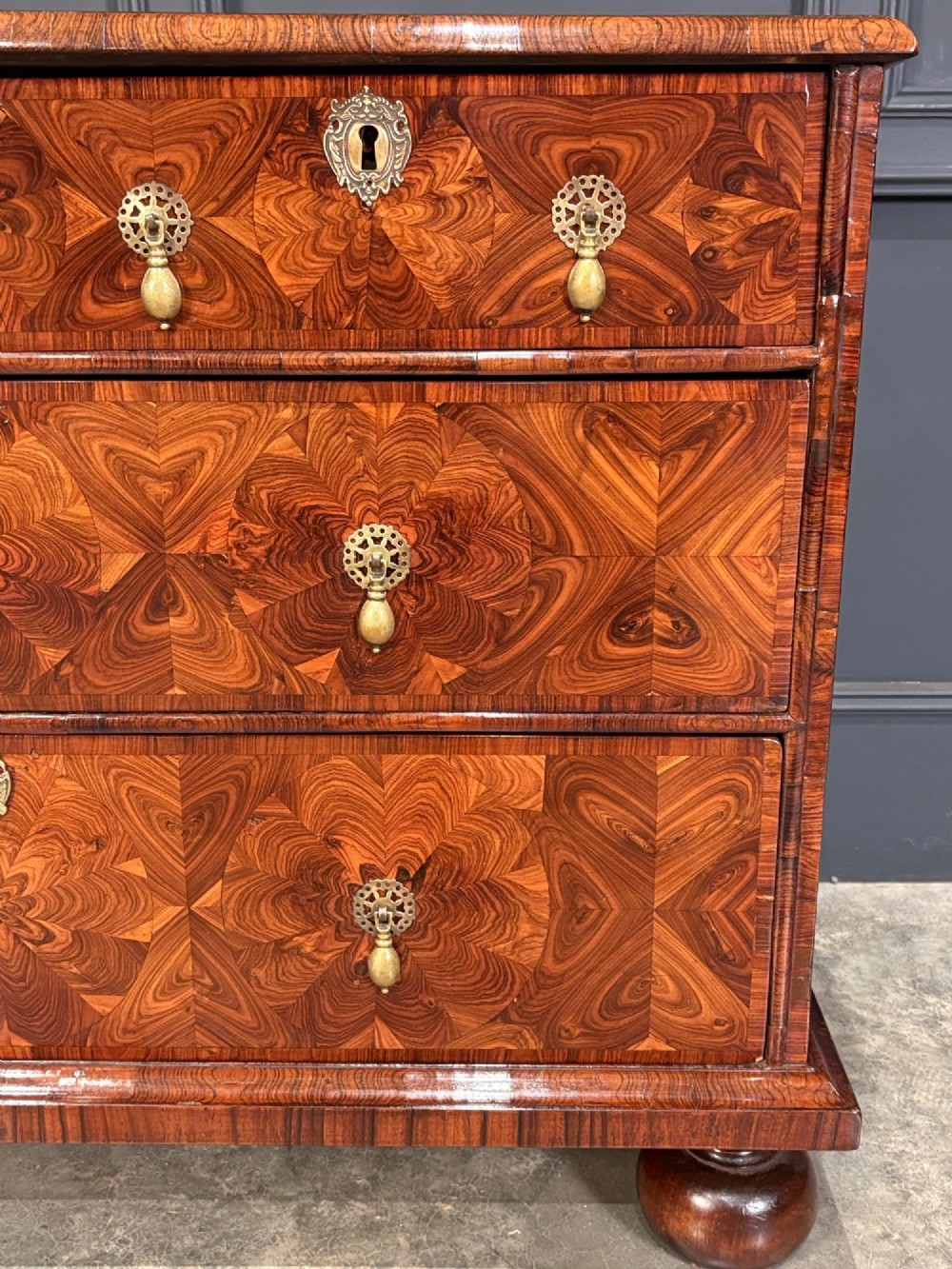 A seventeenth-century kingwood chest of drawers featuring geometric oyster veneering, brass teardrop handles, and turned bun feet. View VII