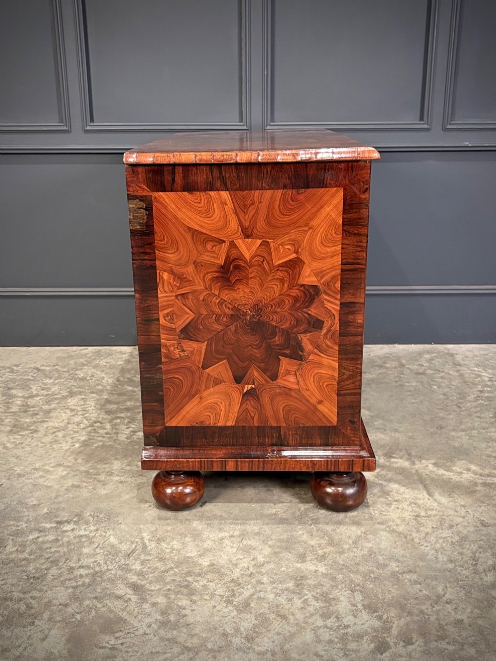 A seventeenth-century kingwood chest of drawers featuring geometric oyster veneering, brass teardrop handles, and turned bun feet. View XII