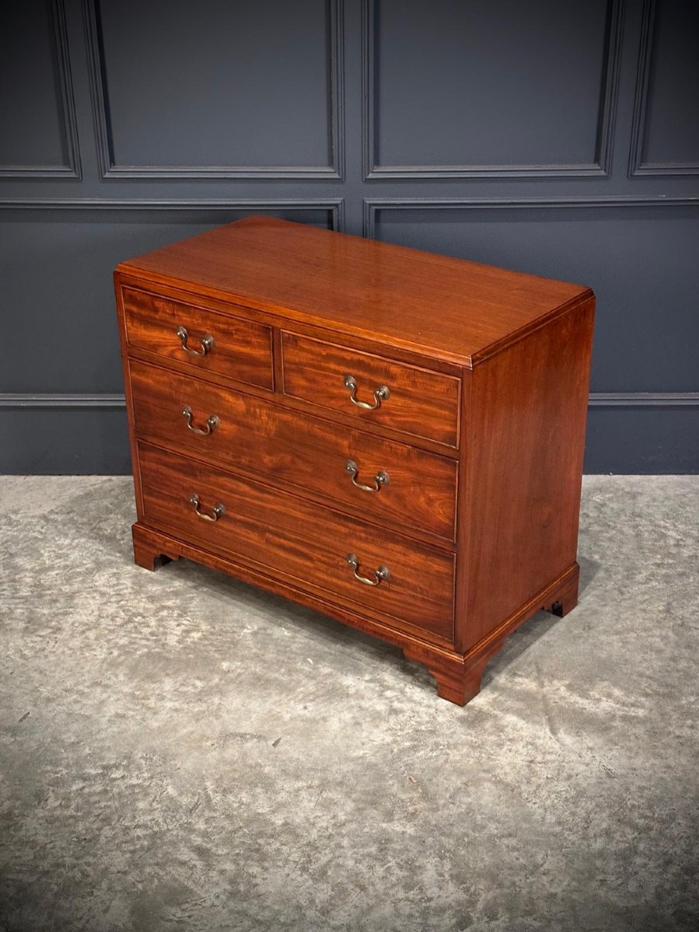 A small mahogany chest of drawers featuring two short over two long drawers with brass swan-neck handles and bracket feet. View V