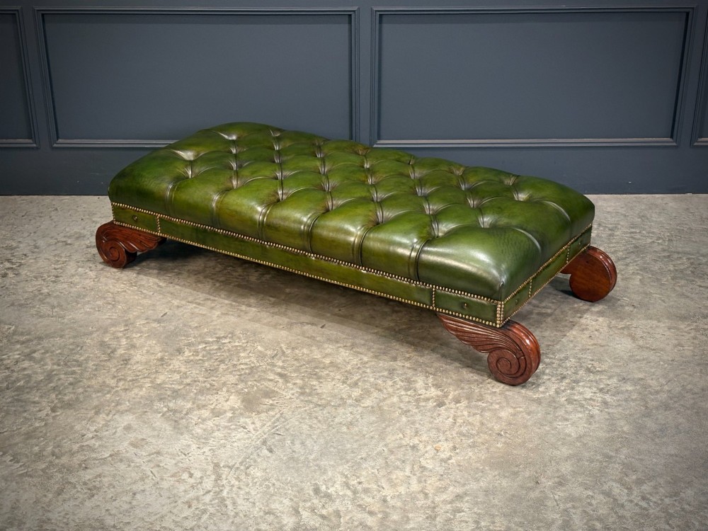 A low rectangular Regency style footstool upholstered in deep-buttoned green leather with brass stud detailing and carved wooden scroll feet. View V