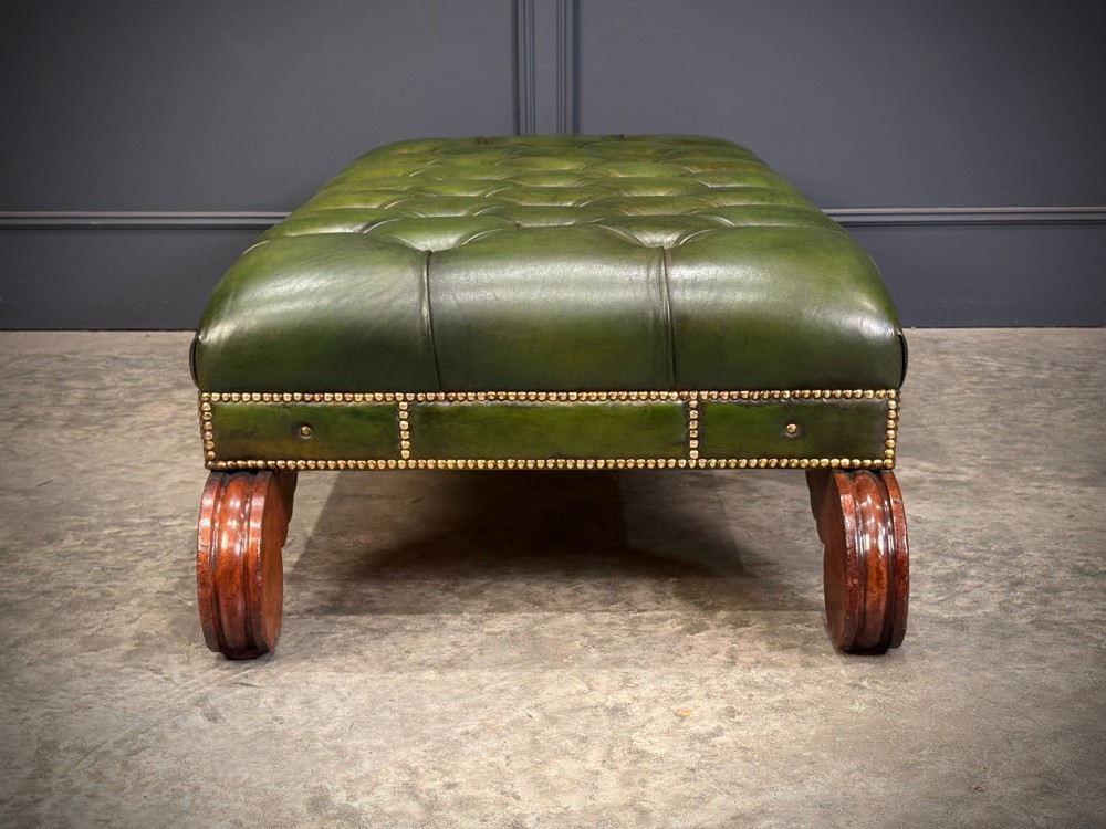 A low rectangular Regency style footstool upholstered in deep-buttoned green leather with brass stud detailing and carved wooden scroll feet. View VIII