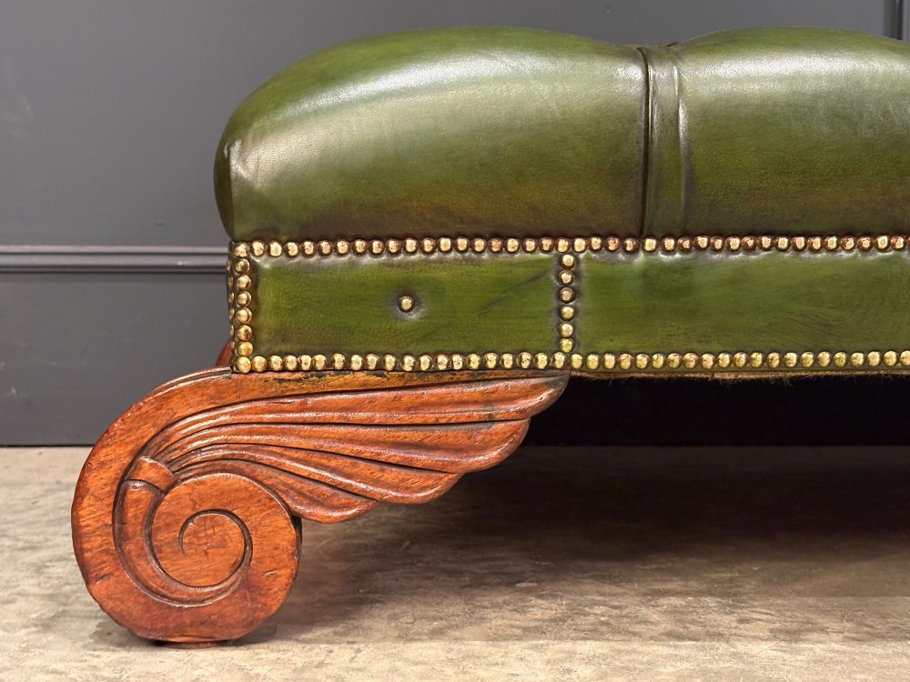 A low rectangular Regency style footstool upholstered in deep-buttoned green leather with brass stud detailing and carved wooden scroll feet. View XI