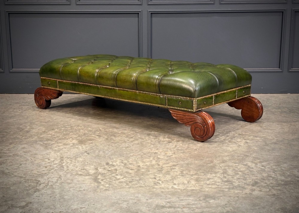 A low rectangular Regency style footstool upholstered in deep-buttoned green leather with brass stud detailing and carved wooden scroll feet. View XII
