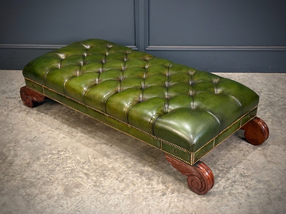 A low rectangular Regency style footstool upholstered in deep-buttoned green leather with brass stud detailing and carved wooden scroll feet. View XIII