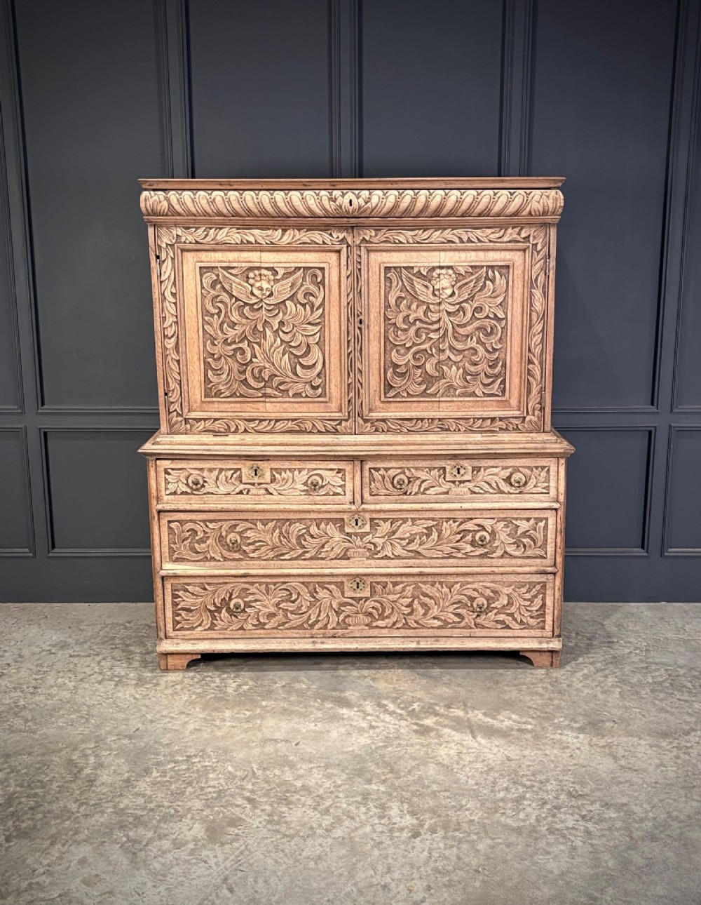 An 18th-century light oak two-piece cupboard on chest featuring detailed hand-carved foliate panels, cherub motifs, and carved drawer fronts. View II