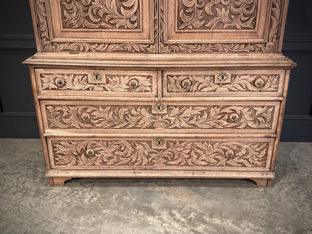 An 18th-century light oak two-piece cupboard on chest featuring detailed hand-carved foliate panels, cherub motifs, and carved drawer fronts. View III