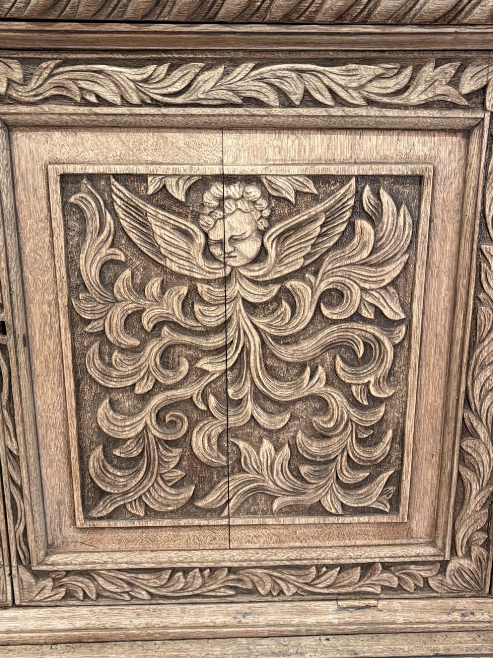 An 18th-century light oak two-piece cupboard on chest featuring detailed hand-carved foliate panels, cherub motifs, and carved drawer fronts. View IV