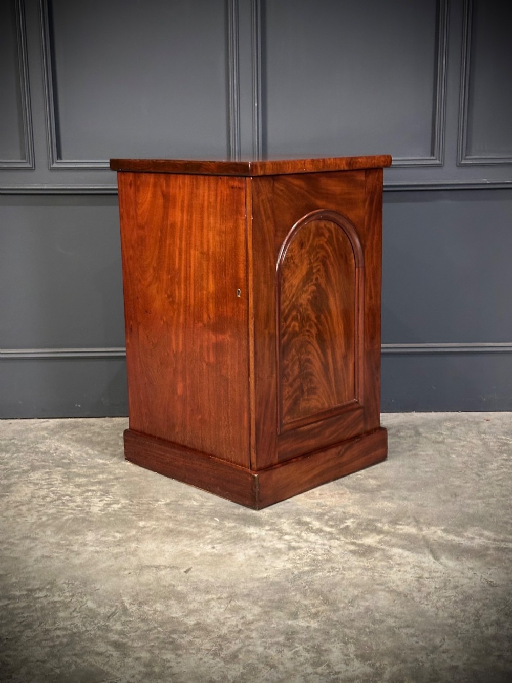 A matching pair of dark flame mahogany bedside cabinets featuring single doors with arched panels resting on solid plinth bases. View VI