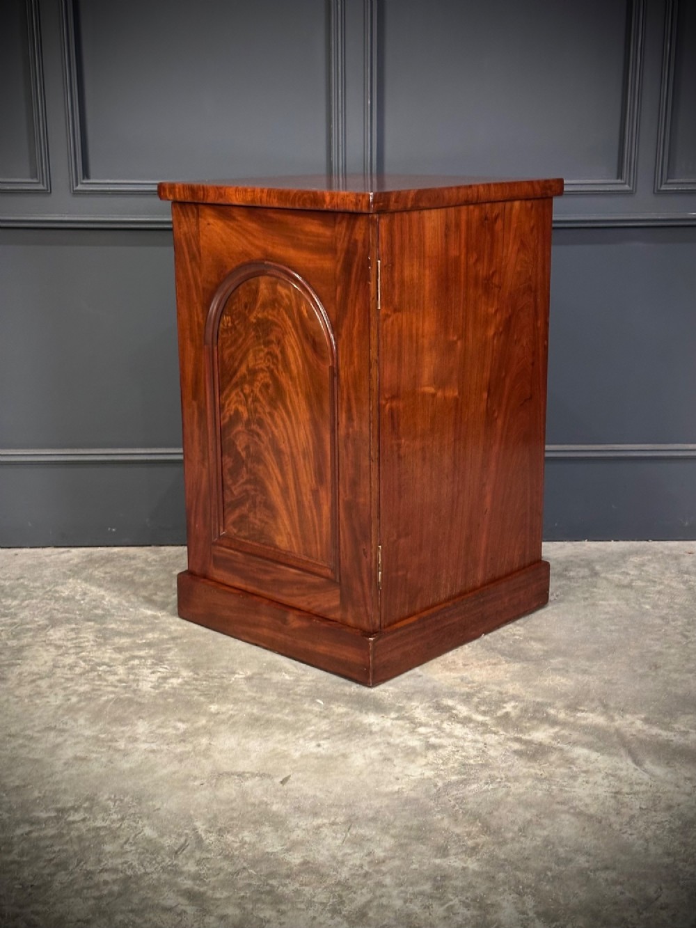 A matching pair of dark flame mahogany bedside cabinets featuring single doors with arched panels resting on solid plinth bases. View IX