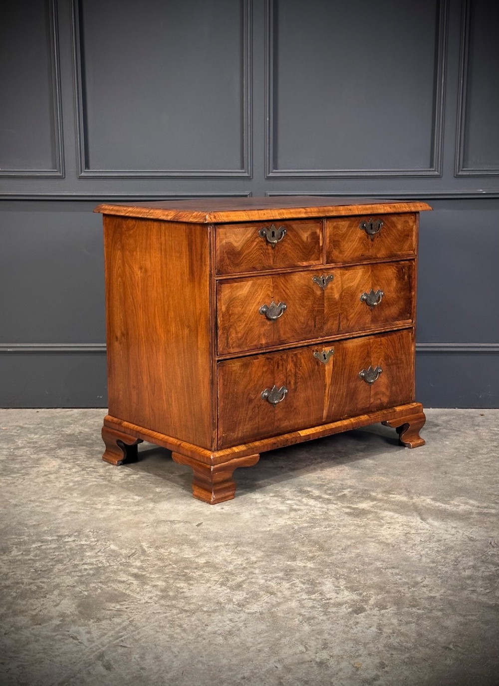 An eighteenth-century Queen Anne walnut chest of drawers featuring two short over two long graduated drawers, brass handles, and shaped bracket feet.