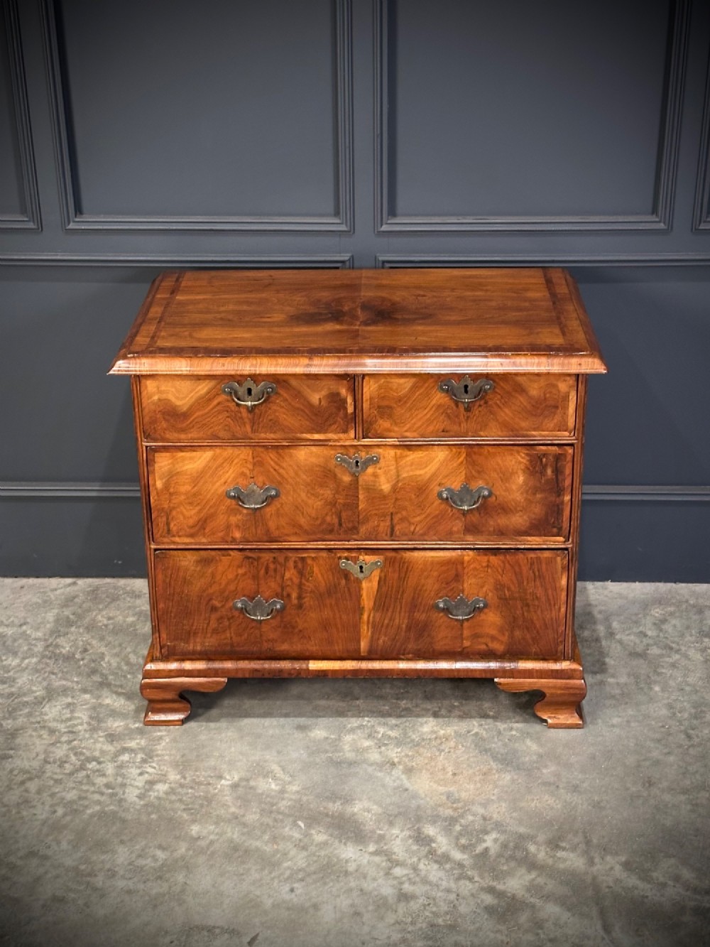An eighteenth-century Queen Anne walnut chest of drawers featuring two short over two long graduated drawers, brass handles, and shaped bracket feet. View V