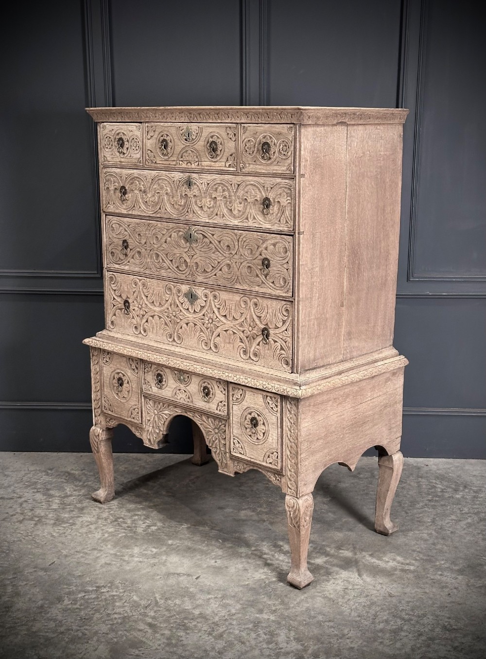 An 18th-century bleached oak chest on stand featuring carved foliage motifs across the drawer fronts and elevated on cabriole legs. View VI