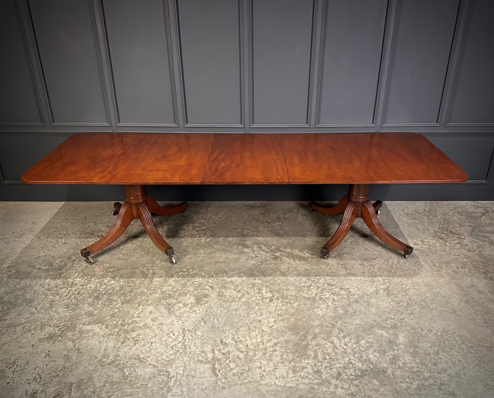 An extended mahogany twin pillar dining table with reeded splayed legs and brass castors.