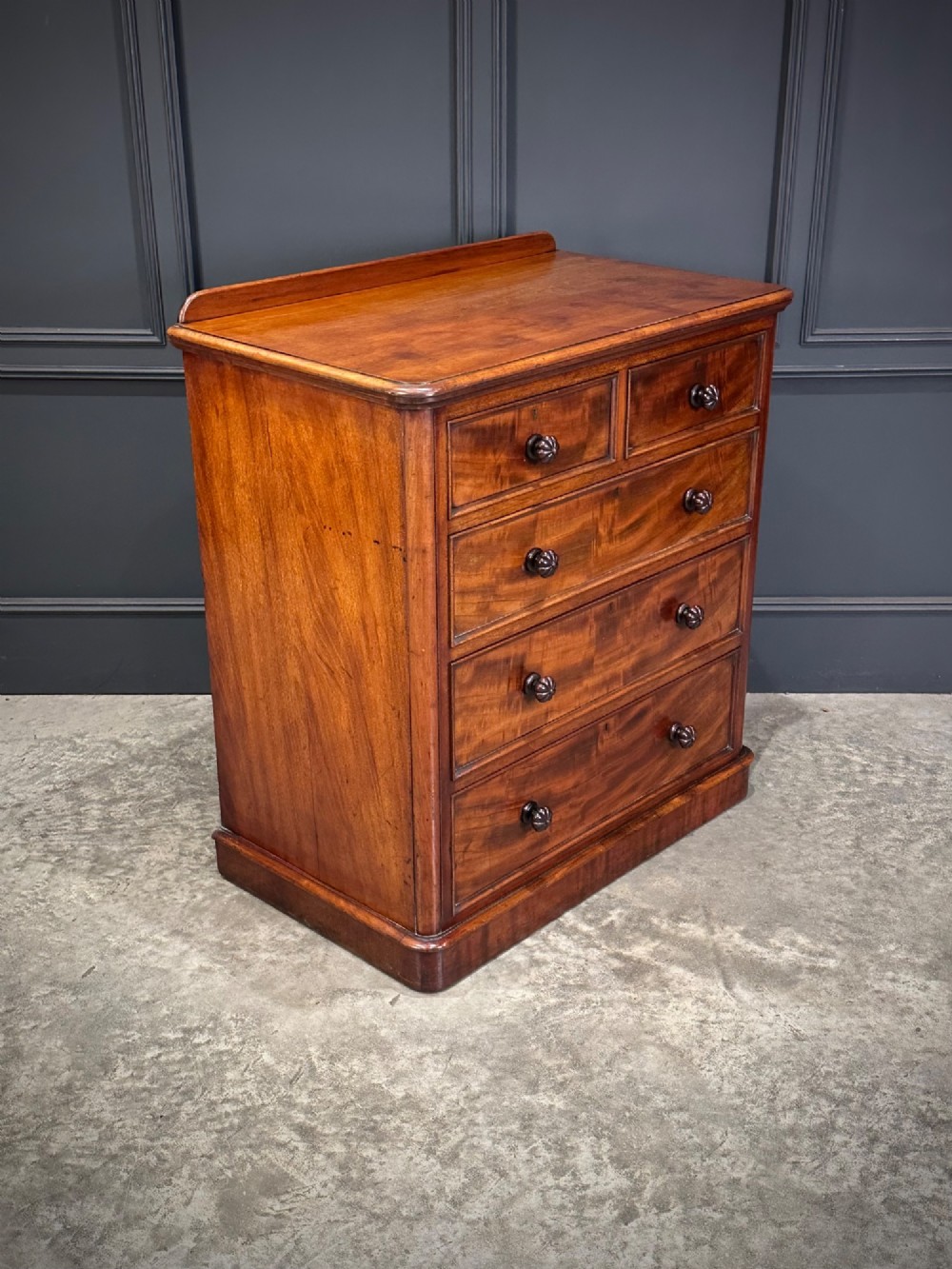 A Victorian flame mahogany chest of drawers featuring two short over three long drawers with turned knobs and a plinth base. View II