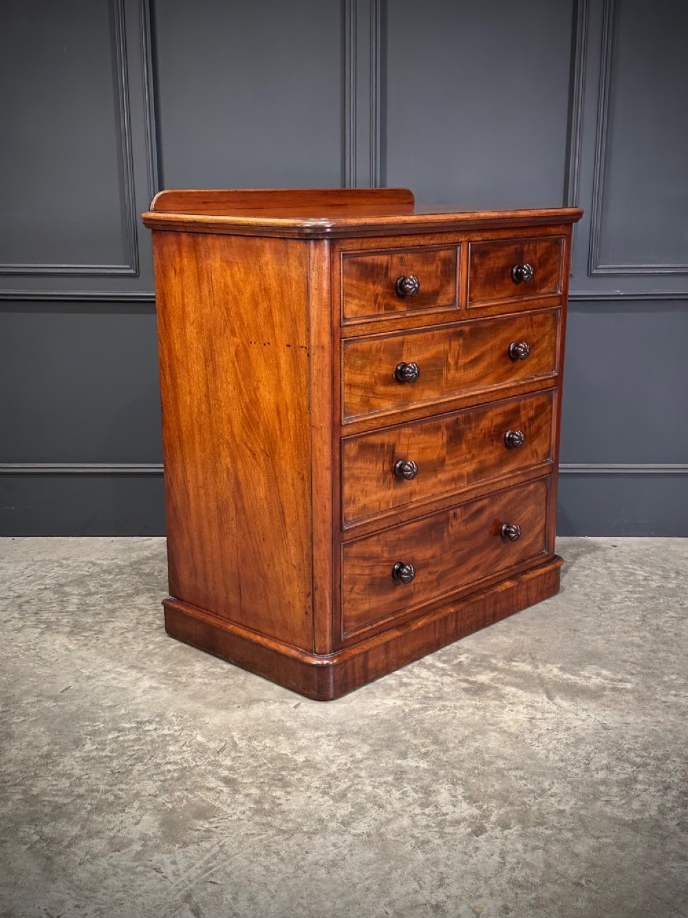 A Victorian flame mahogany chest of drawers featuring two short over three long drawers with turned knobs and a plinth base. View III