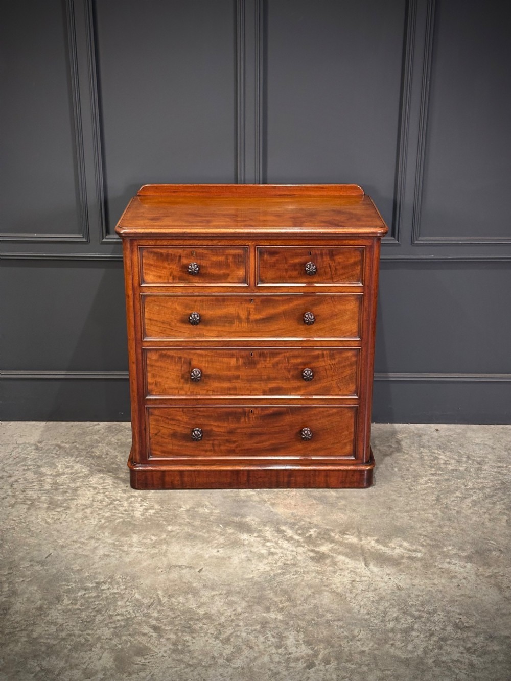 A Victorian flame mahogany chest of drawers featuring two short over three long drawers with turned knobs and a plinth base. View IV
