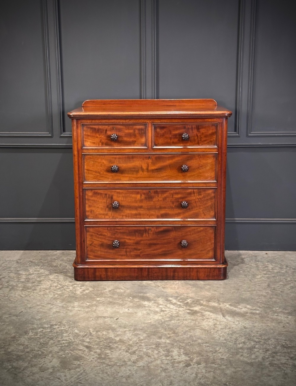 A Victorian flame mahogany chest of drawers featuring two short over three long drawers with turned knobs and a plinth base.